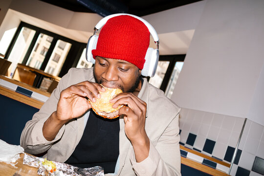 Young man eating hamburger wearing headphones in restaurant