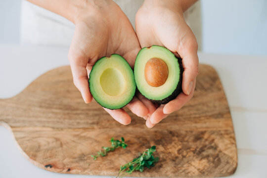 Hands holding fresh avocado halves showing seed and texture