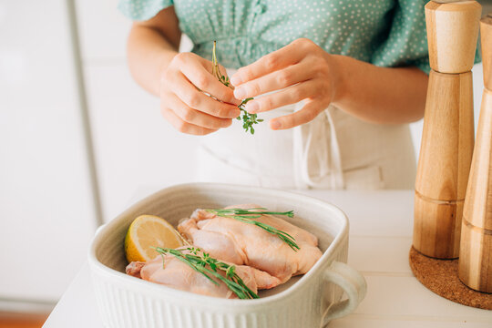 Close-up of hands seasoning raw chicken with fresh herbs and lem