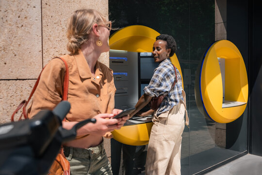 Happy friends withdrawing cash in the city ATM 