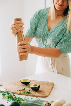 Woman seasoning fresh avocado halves with pepper mill in bright 