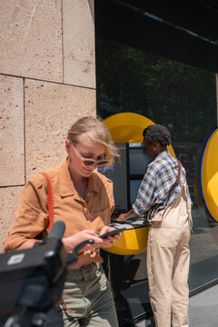 Woman using ATM while another person waiting in queue 