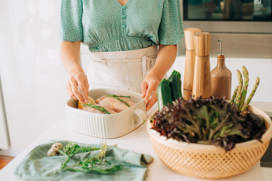 Woman preparing chicken with fresh vegetables and herbs in kitch