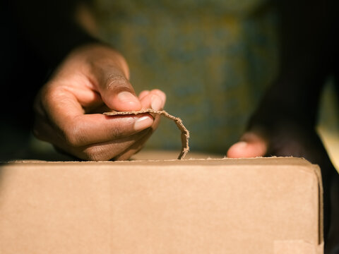 Hands Open a Cardboard Box in a Sunny Home