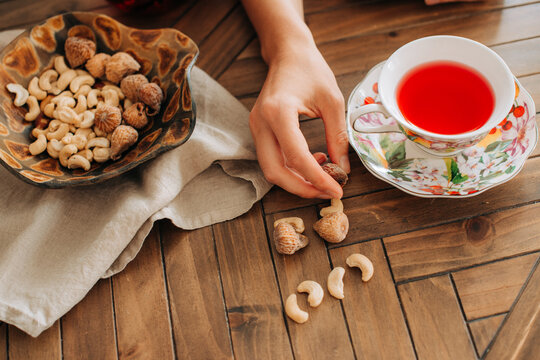 Hand picking nuts next to cup of herbal tea on wooden table