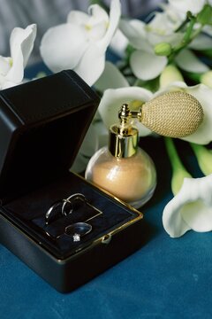 Close up of box with wedding rings, perfume and flowers on table