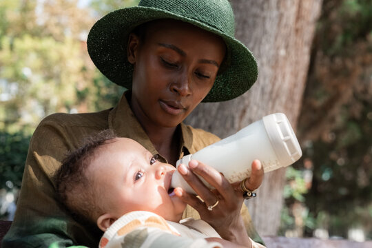 Mother Feeds Baby With Bottle in Park on a Sunny Day