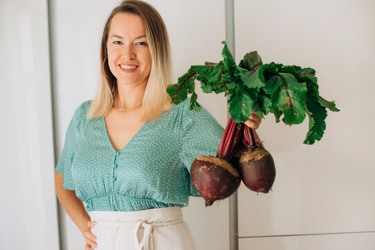 Woman posing with fresh beets in modern kitchen promoting health