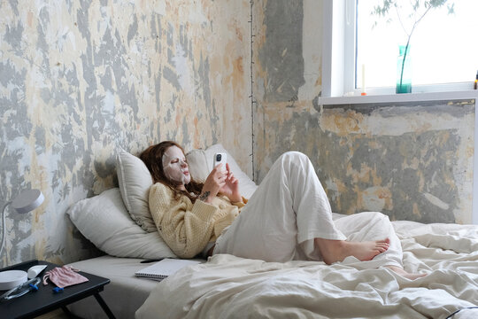 The girl with the phone is lying on the bed.