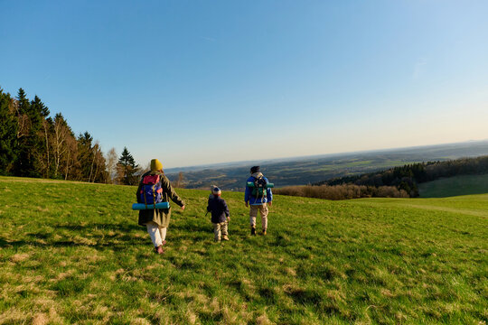 Family hiking with backpacks across sunny hillside