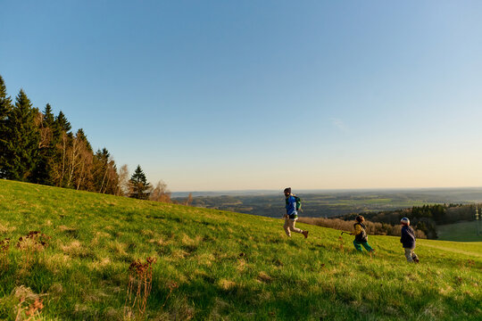 Father and children running across sunny hillside