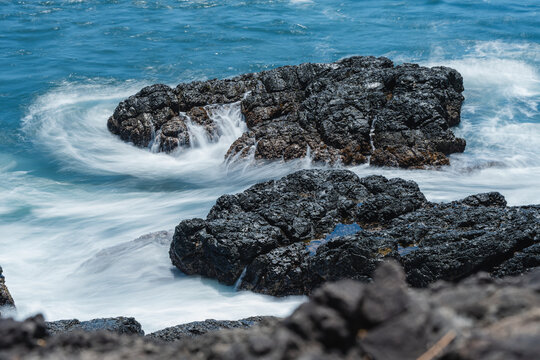 Ocean waves swirling around dark volcanic rocks at coast