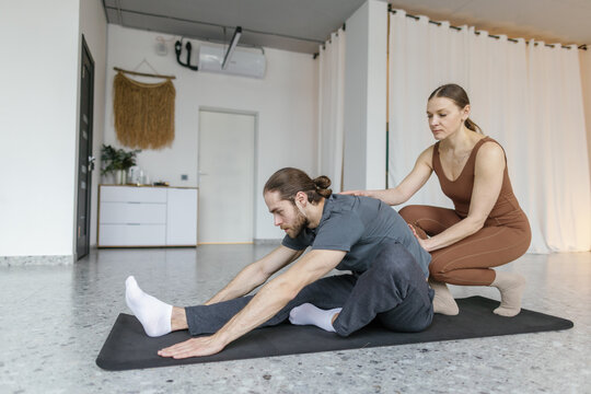 Side of trainer teaching man practicing yoga in Janu Sirsasana pose