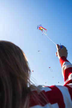 Young woman flying a colorful kite with numerous kites in sky