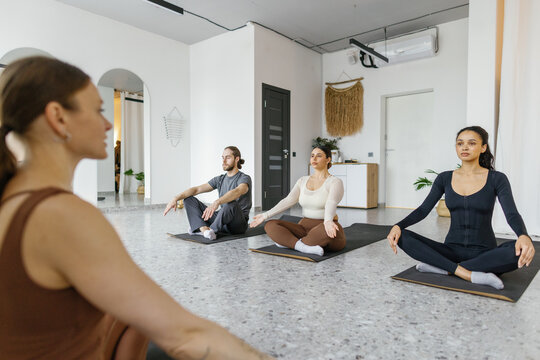 Female trainer teaching people practicing yoga in Baddha Konasana pose