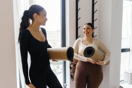 Pleased woman looking at black joyful girlfriend in fitness studio