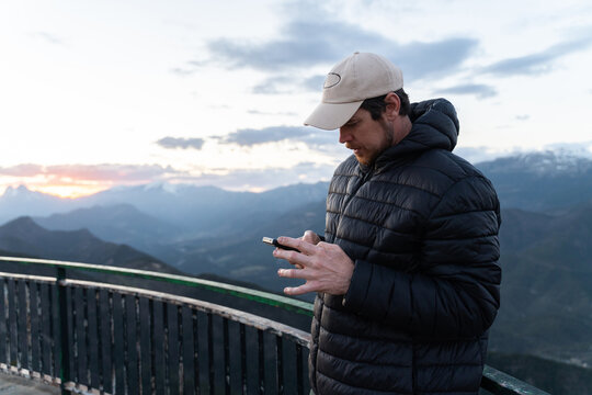 Man Checks Phone on Mountain During Sunset