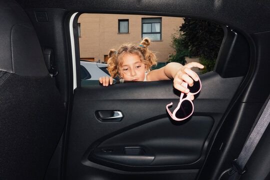 Girl looking through car window holding heart shaped sunglasses
