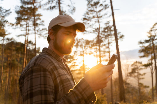 Man Using Phone in Forest During Sunset 