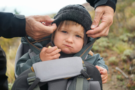 Child in Backpack Carrier in Nature With Adult's Hands Adjusting Gear