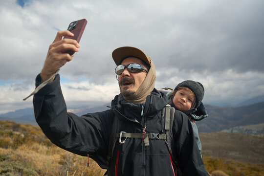 Man Takes Selfie With Child on His Back During Hike in Nature