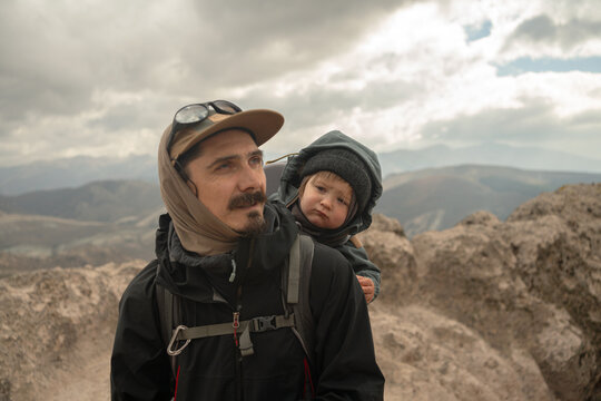 Father Carries Child During Mountain Hike on Cloudy Day