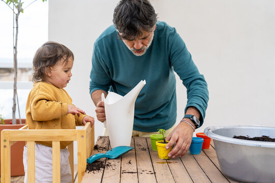 Father Guiding Baby While Watering Plants Together