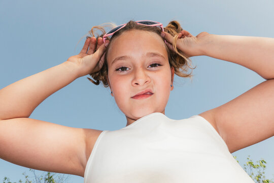 Girl with highly expressive face touching her sunglasses outdoors