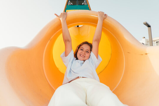 Girl sliding down orange playground slide with arms raised