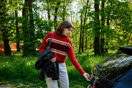 Casual woman opens car trunk in nature