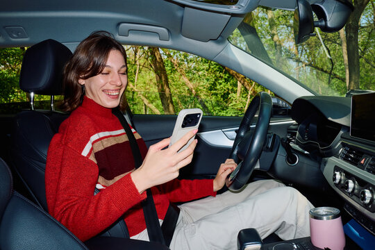 Woman drives her car, looking at a mobile phone