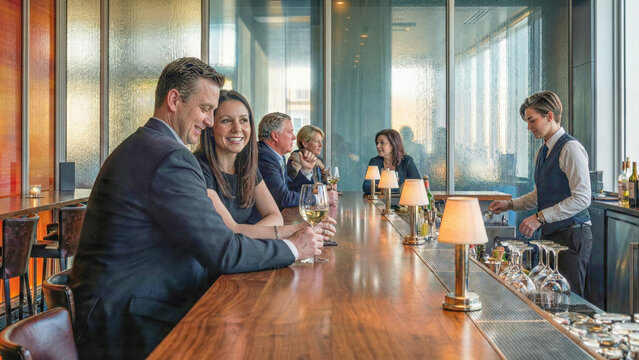 Professionals socializing with wine at an upscale hotel bar or lounge while a bartender prepares drinks.