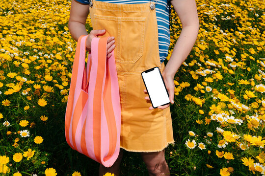 Person Holding a Phone with White Screen in a Field of Yellow Flowers