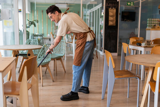 Young employee sweeping cafe floor preparing for work