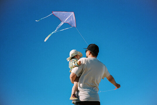 Father with baby flying a kite opposite the blue sky