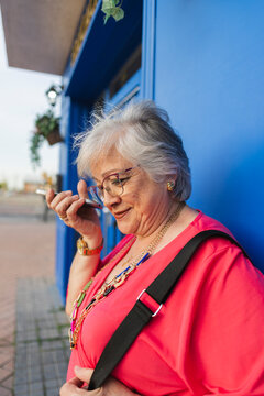 Senior woman using voice assistant on phone outdoors