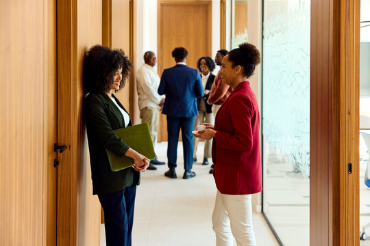 Two women chatting in a busy office corridor