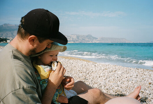 Young father feeding baby near the sea