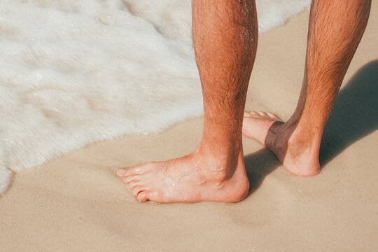 Man standing barefoot beach shoreline with ocean water