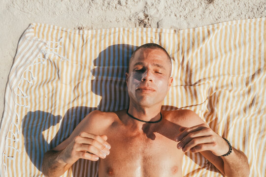 Man lying on beach towel wearing sunscreen