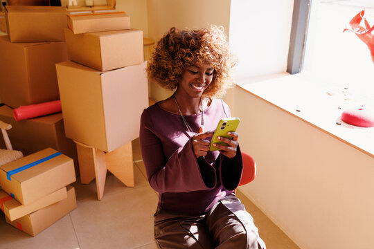 Woman using phone for ecommerce business with moving boxes