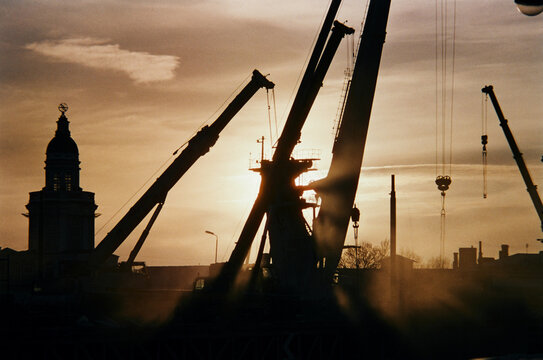 Cranes work during sunset near a tall tower