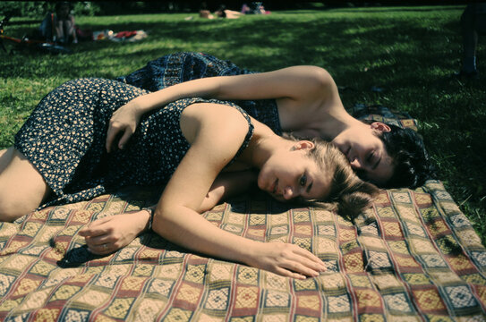 Two friends lie together on a blanket in a park
