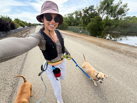 dog walker selfie asian woman walking two dogs on leash smiling 