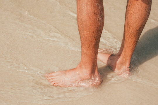 Man standing barefoot beach shoreline with ocean water