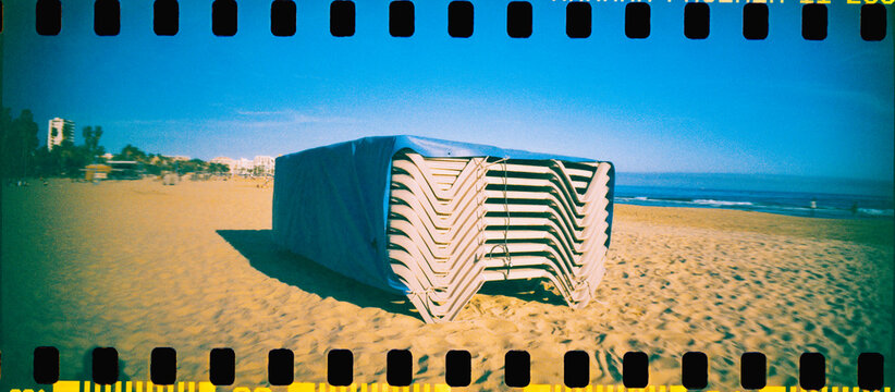 stacked beach loungers under a blue tarp by the sea, 35mm film