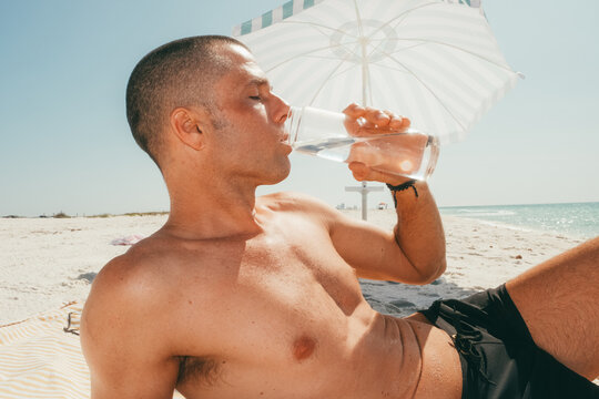 Man drinking water relaxing under beach umbrella