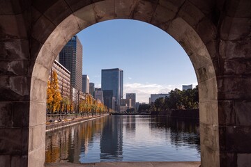 石造りのアーチ越しに望む皇居外苑の水辺と東京の高層ビル群 © irukuji
