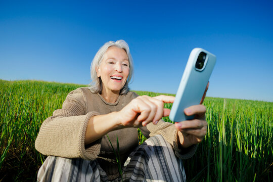 Happy woman using smartphone sitting in green field