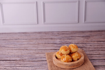 Fototapeta premium Kue Nastar or Golden pastries rest in a wooden bowl. Bowl sits atop burlap on aged wood. Warm tones evoke comfort and homemade charm. Ideal for food blogs, bakery ads, or cozy lifestyle content